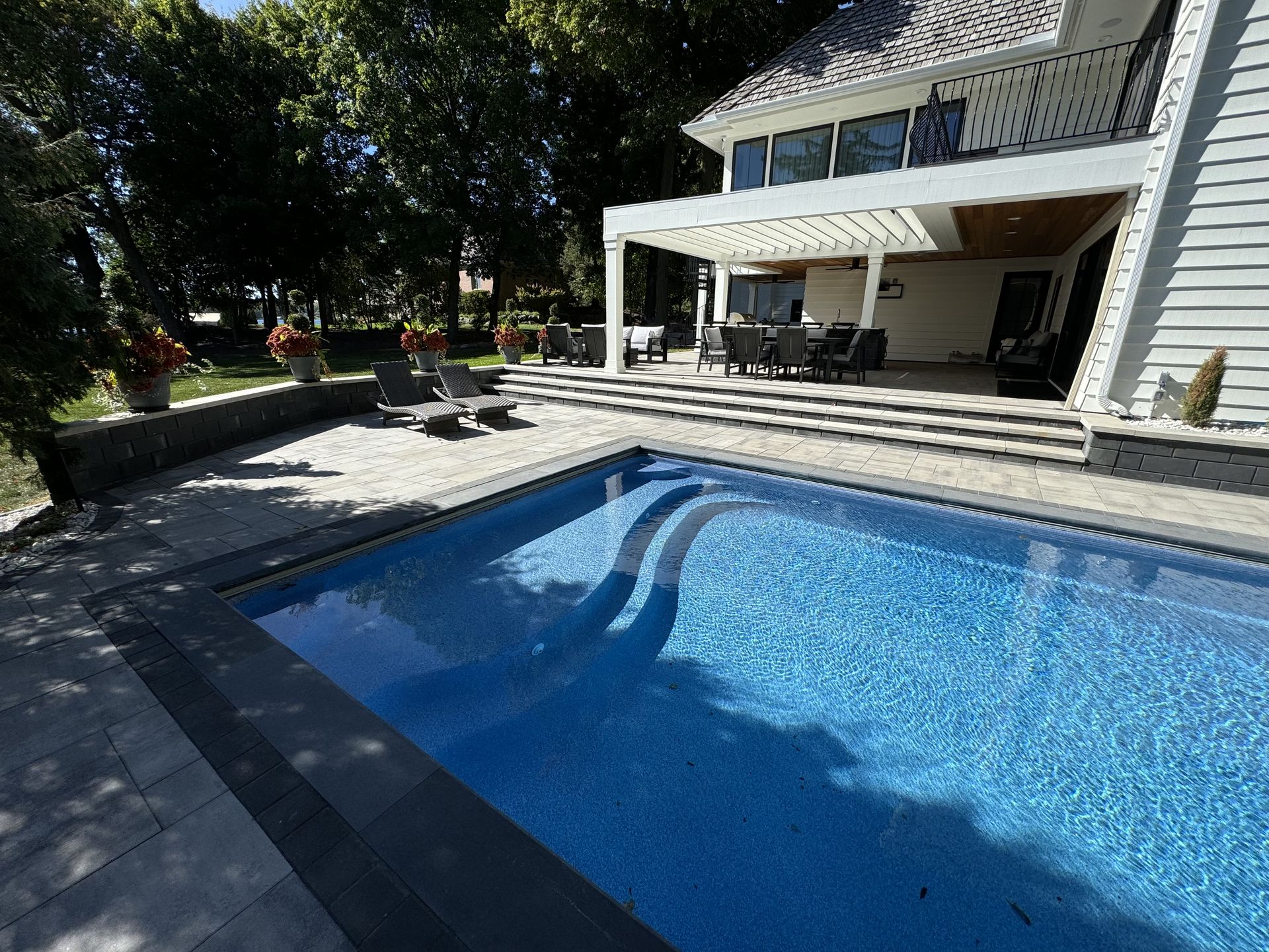 A beautifully designed custom pool featuring surrounding natural stone pavers,  and massive outdoor living area; all perfectly tailored to fit existing outdoor space.