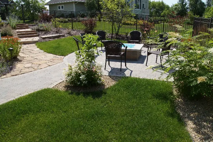 A custom built natural stone fireplace, nestled between lush green lawn and natural stone paver patio.