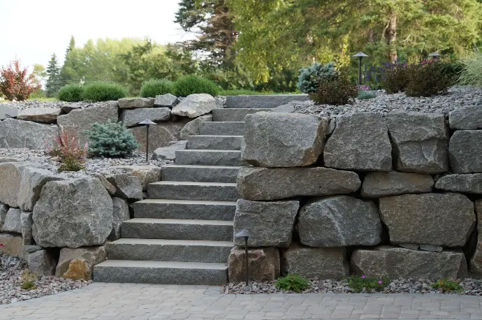 A stacked natural stone retaining wall running alongside a stone paver stair walkway, offering both support and beauty.