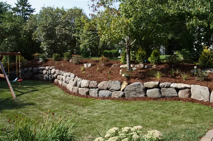 A tiered natural stone retaining wall, designed to hold back soil while showcasing vibrant plant life.