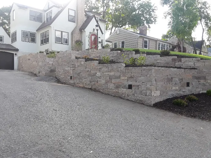 A tiered natural stone retaining wall, designed to hold back soil while showcasing vibrant plant life.