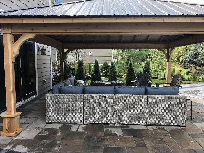 This custom built wooden pavilion sits a top a natural stone paver patio with modern outdoor living furniture, creating a warm outdoor living space.