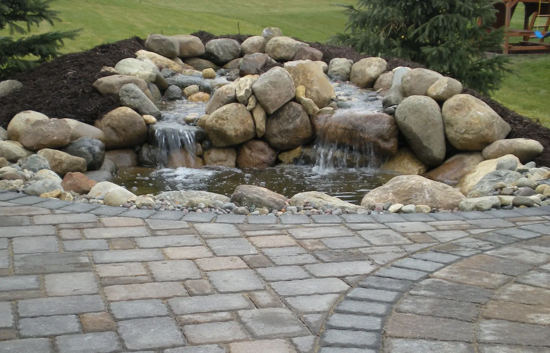 A serene natural stone waterfall cascading into a clear pond, creating a peaceful and tranquil outdoor atmosphere.