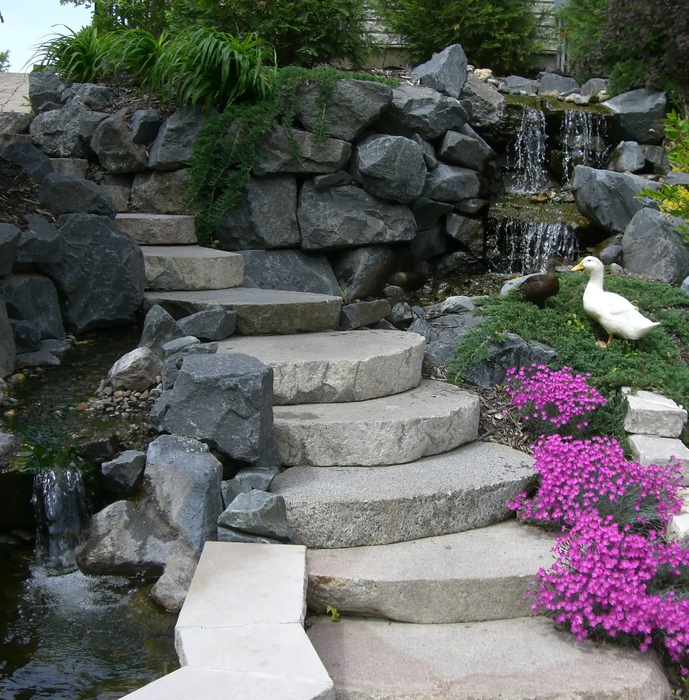 A serene natural stone waterfall cascading into a clear pond, creating a peaceful and tranquil outdoor atmosphere.